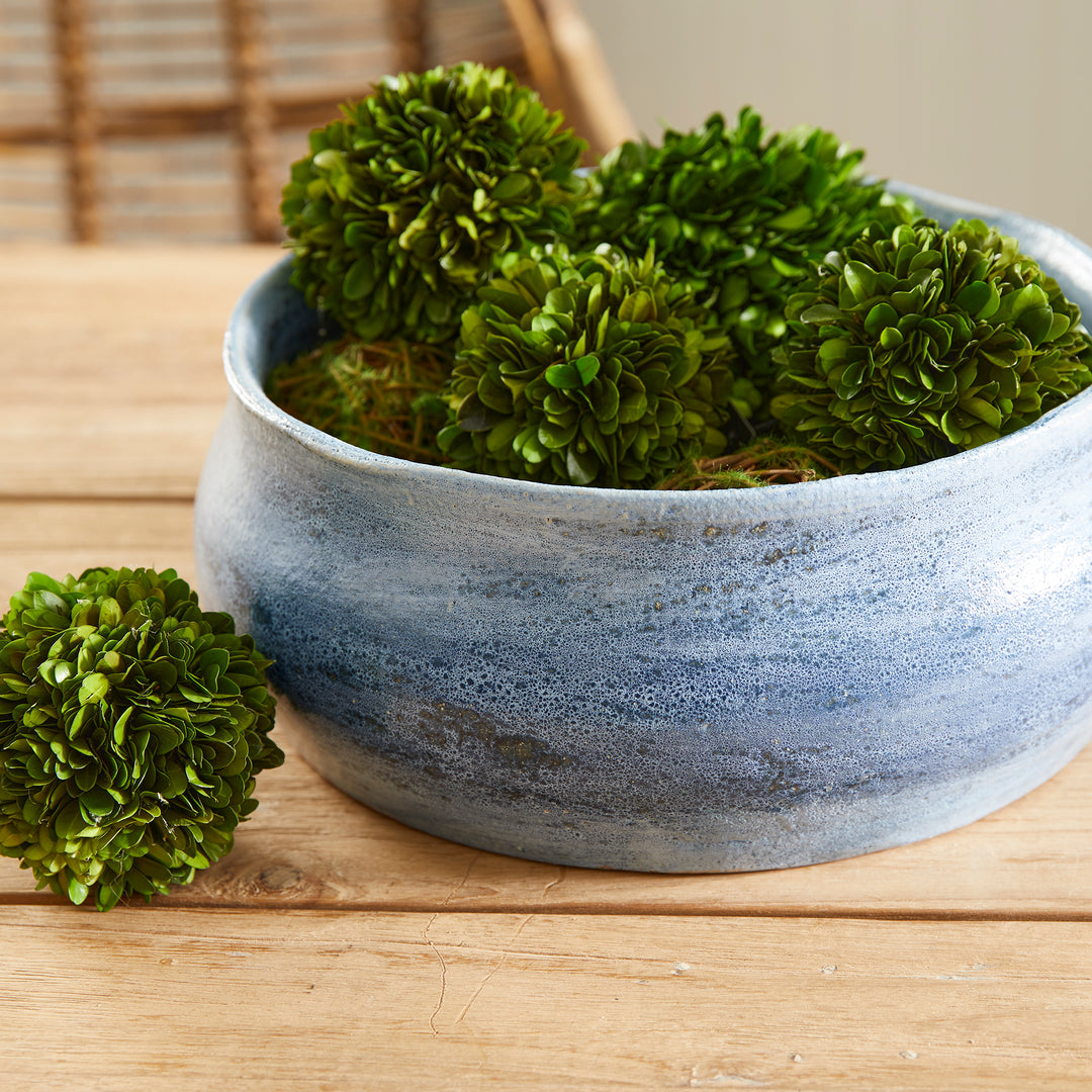 Blue ceramic bowl filled with green decorative spheres on a wood table, used as a centerpiece or tabletop accent – Coastal Transitional.
