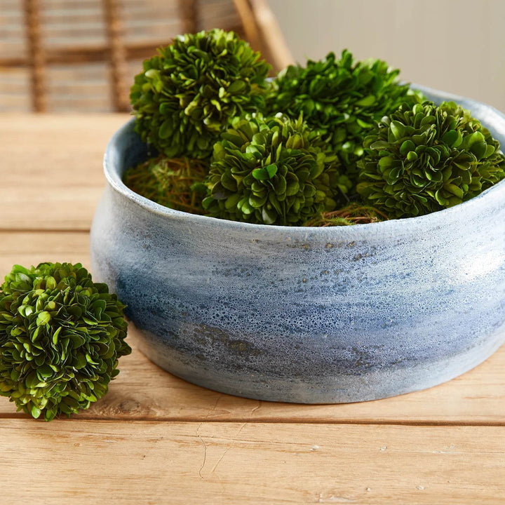 Blue ceramic bowl filled with green decorative spheres on a wood table, used as a centerpiece or tabletop accent – Coastal Transitional.