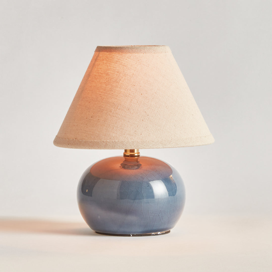 Blue ceramic mini table lamp illuminated beneath its cream linen shade, shown on a plain backdrop - Coastal Transitional