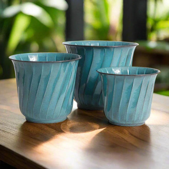 Top view of blue enamel metal planters in three sizes, shown on a modern wood table with soft shadows and indoor lighting.