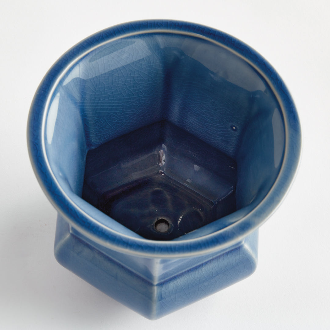 Overhead view into a blue glazed ceramic planter showing its faceted interior and central drainage hole on white, Traditional