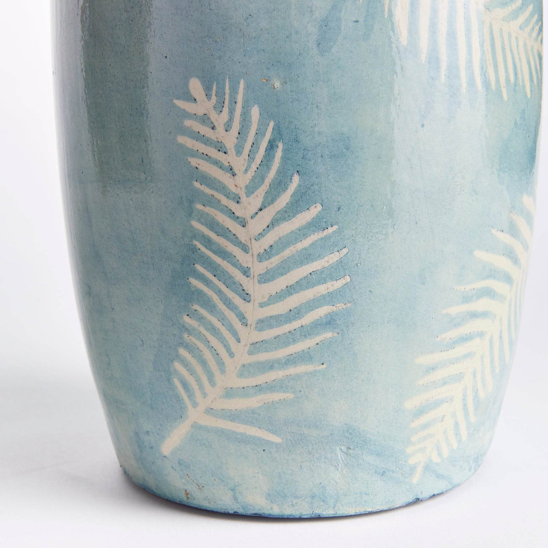 Hand painted white fern detail on matte blue vase surface in close-up view