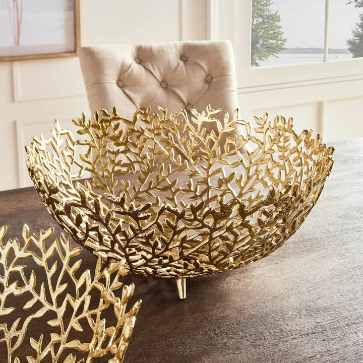 Set of gold decorative bowls in leaf motif, shown on a wood tabletop with soft upholstered seating.