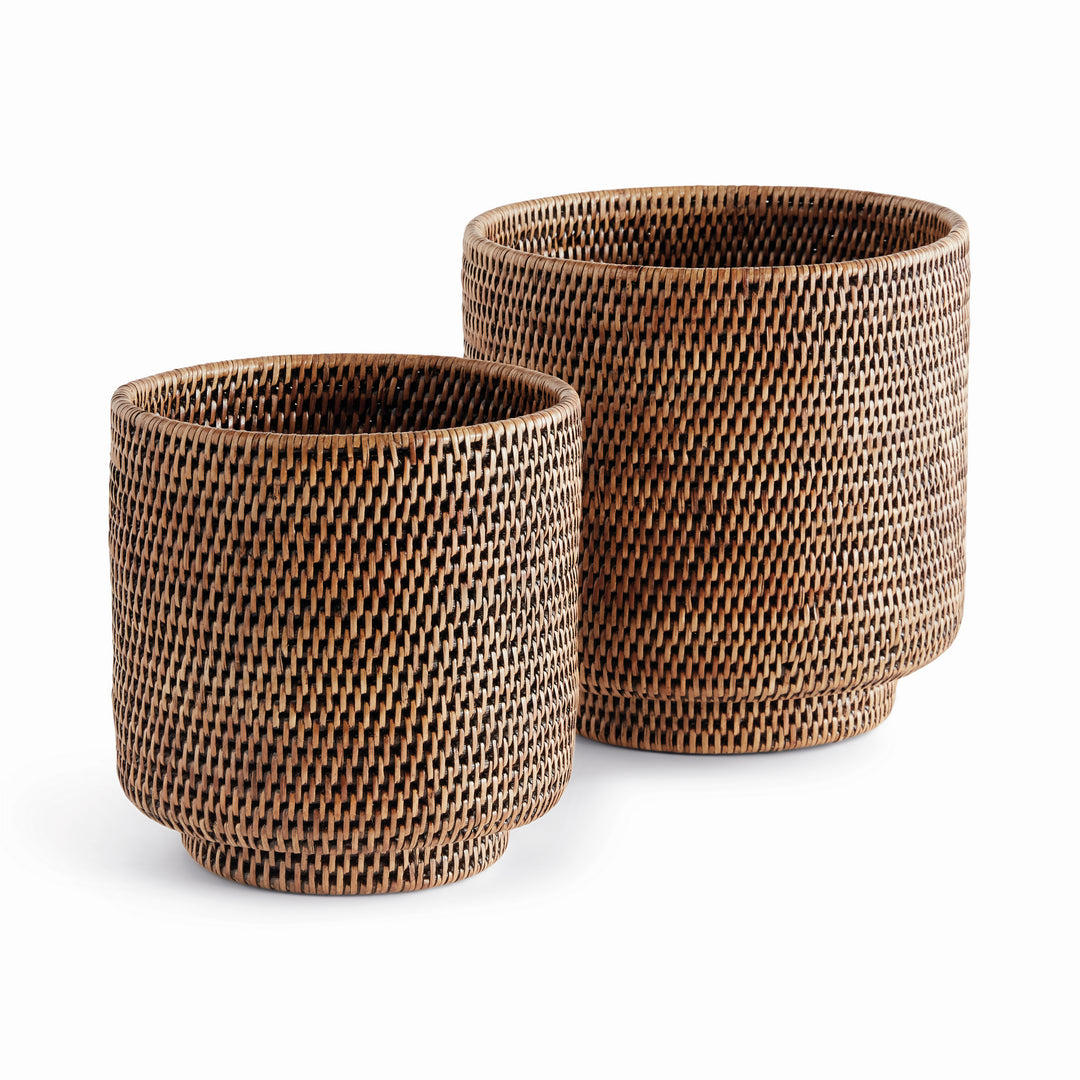 Brown rattan cachepots in two sizes with cylindrical woven sides and small round feet, shown on white - Coastal Transitional