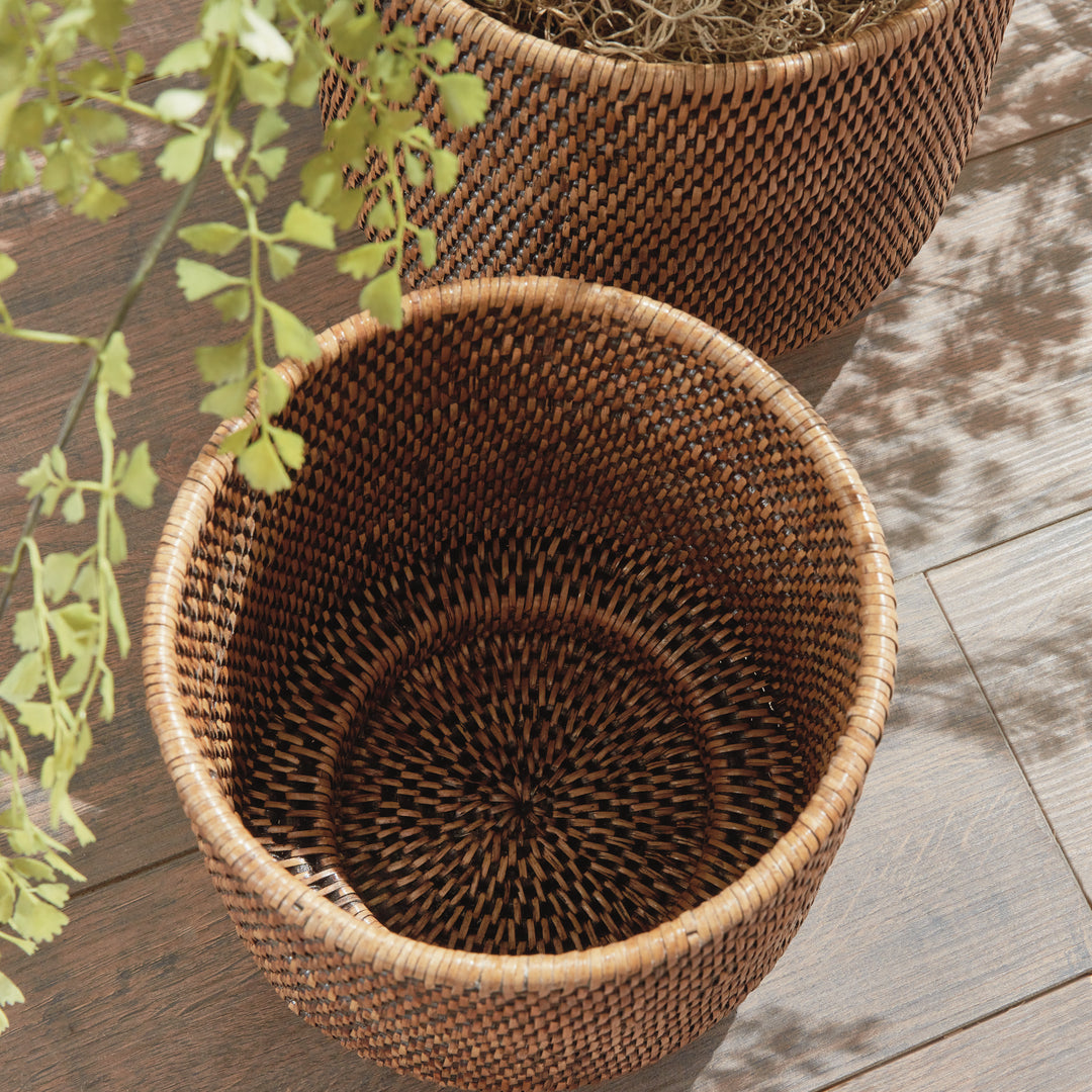 Brown rattan cachepots viewed from above on a wooden floor, showing the woven interior beside foliage - Coastal Transitional