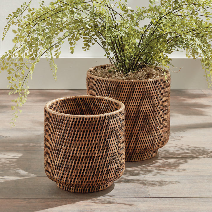 Brown rattan cachepot set styled on a wooden floor, with foliage rising from the larger woven pot - Coastal Transitional