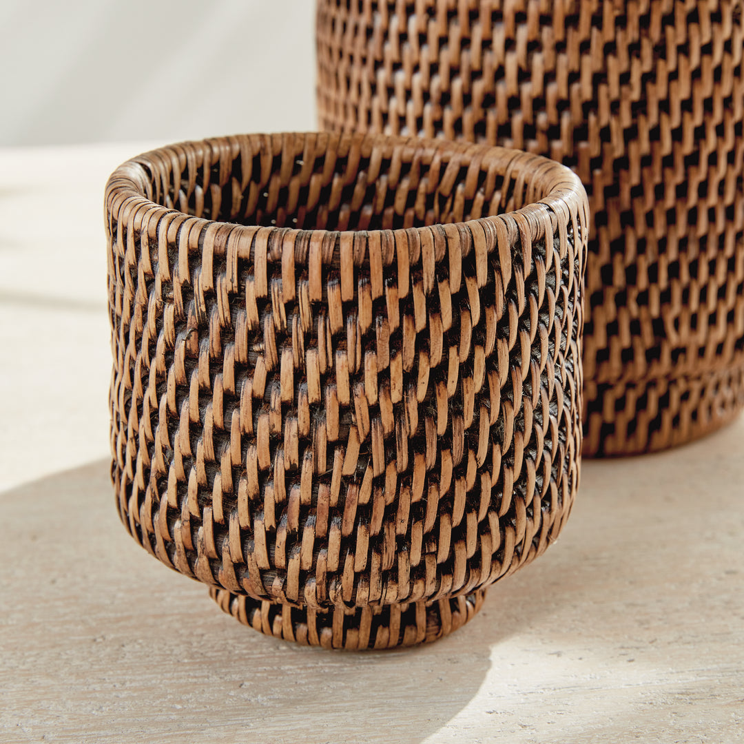 Brown rattan cachepot detail showing the rounded rim and close weave, with a second pot behind it - Coastal Transitional