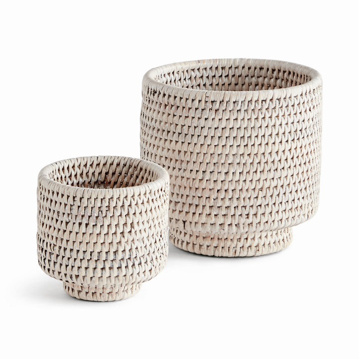 Whitewash rattan cachepots in two sizes with cylindrical woven sides and round feet, shown on white - Coastal Transitional