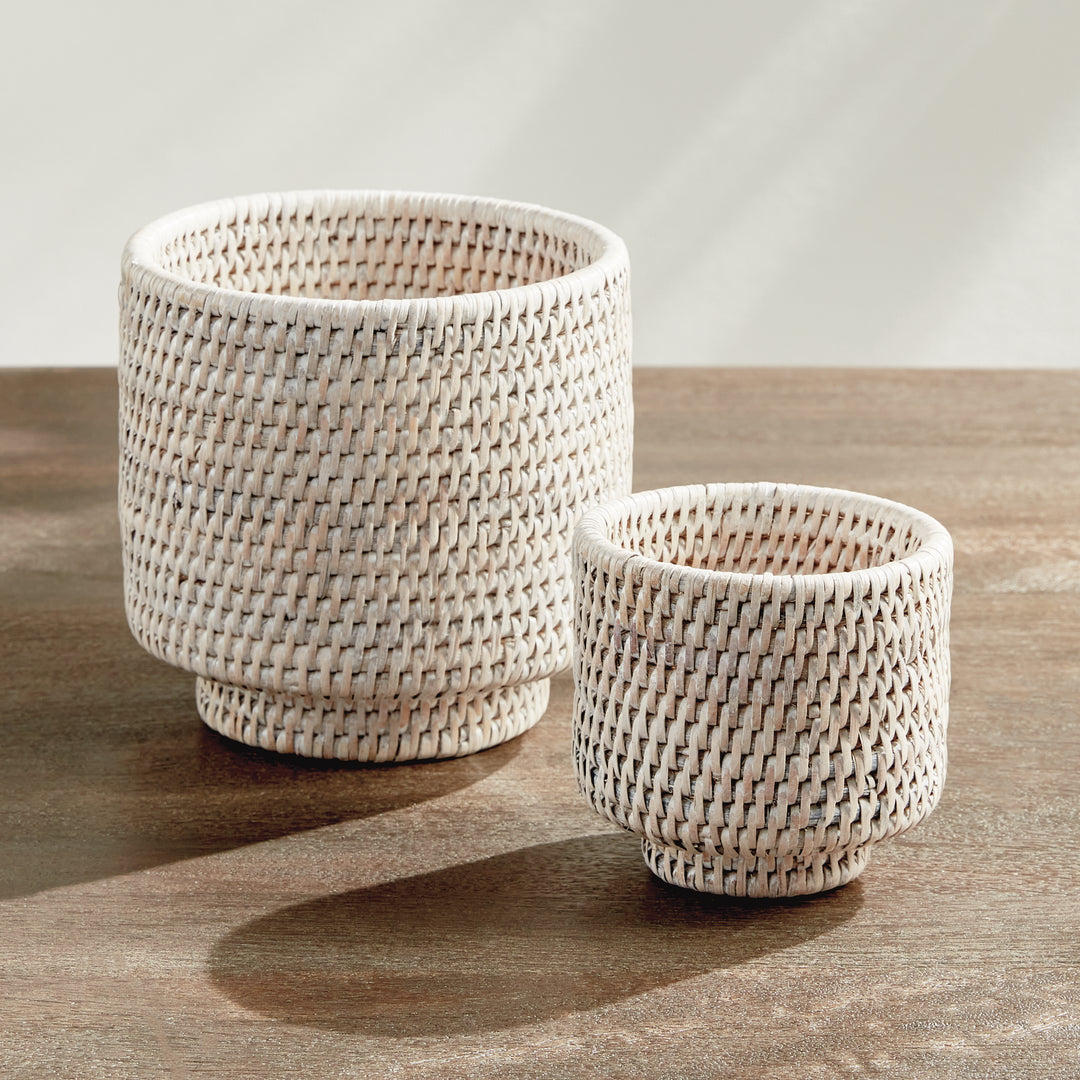 Whitewash rattan cachepot pair on a stone tabletop, shown empty with woven sides and low raised feet - Coastal Transitional