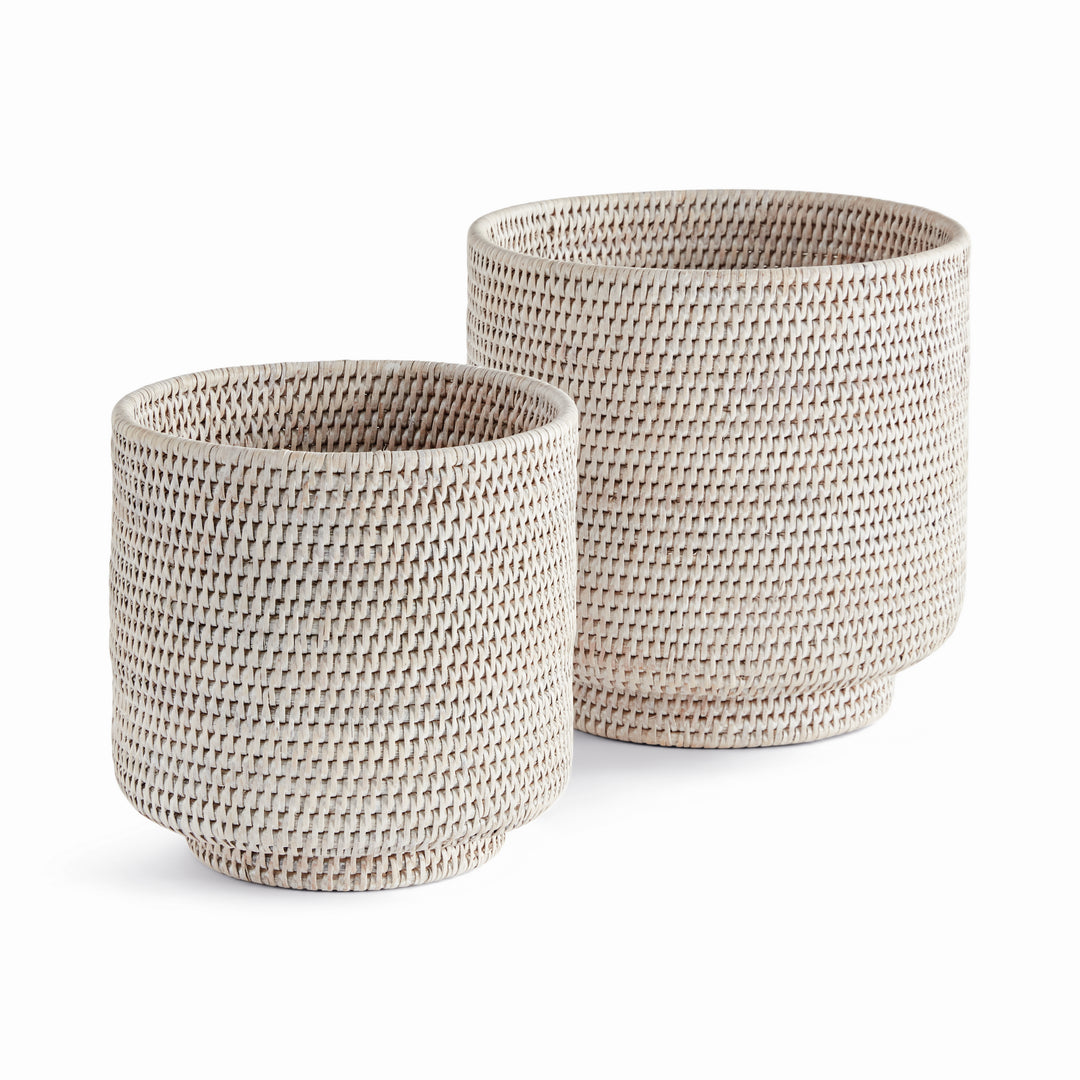 Whitewash rattan cachepots in two sizes with cylindrical woven sides and round feet, shown on white - Coastal Transitional