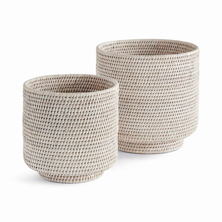 Whitewash rattan cachepots in two sizes with cylindrical woven sides and round feet, shown on white - Coastal Transitional