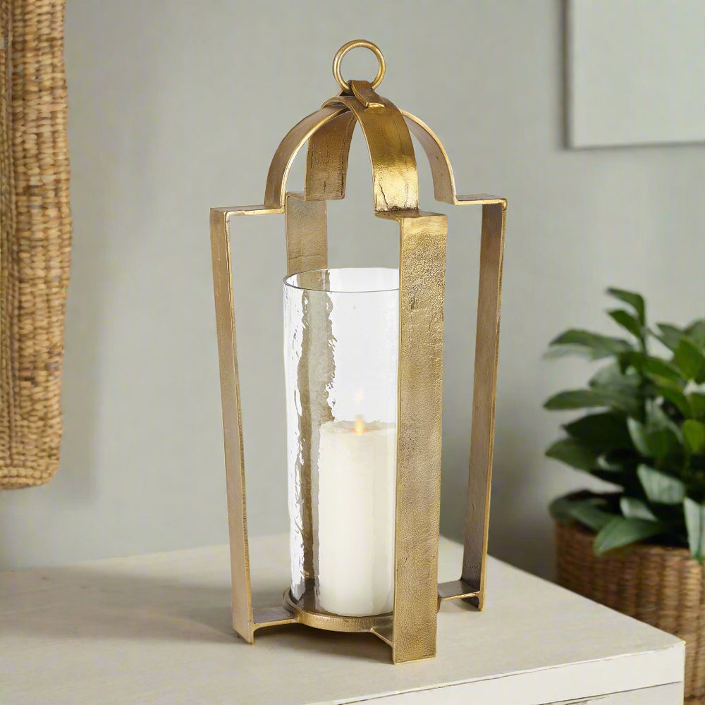 Modern brass hurricane lantern with hammered glass and candle displayed on a sideboard in a transitional space.
