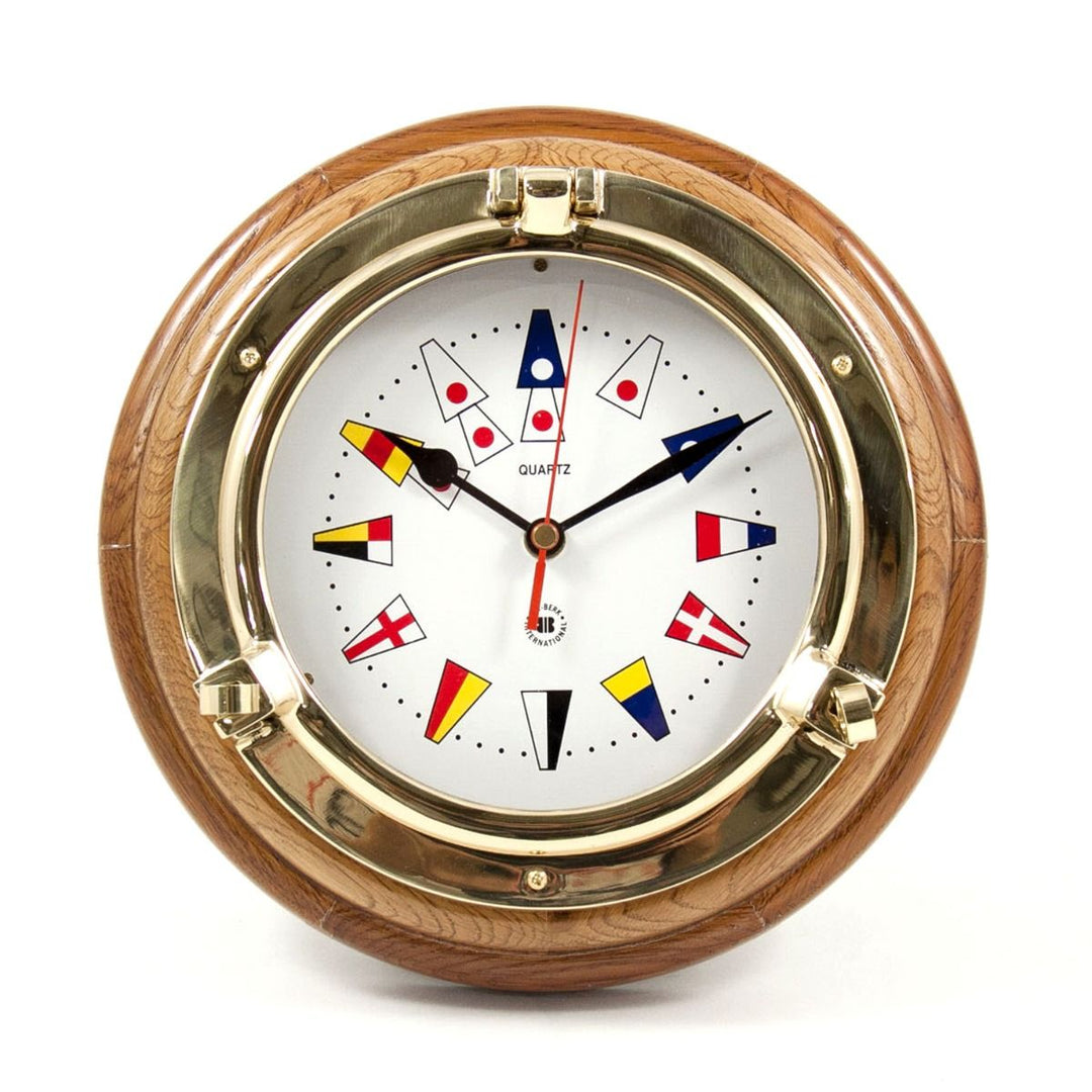 Brass porthole wall clock with nautical flags dial and oak wood frame shown front view for coastal yacht decor style