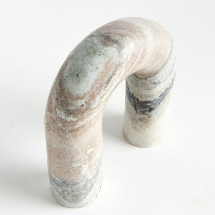 Angled view of a marble arch sculpture with curved top, brown and white veining and two upright stone legs. Modern Organic
