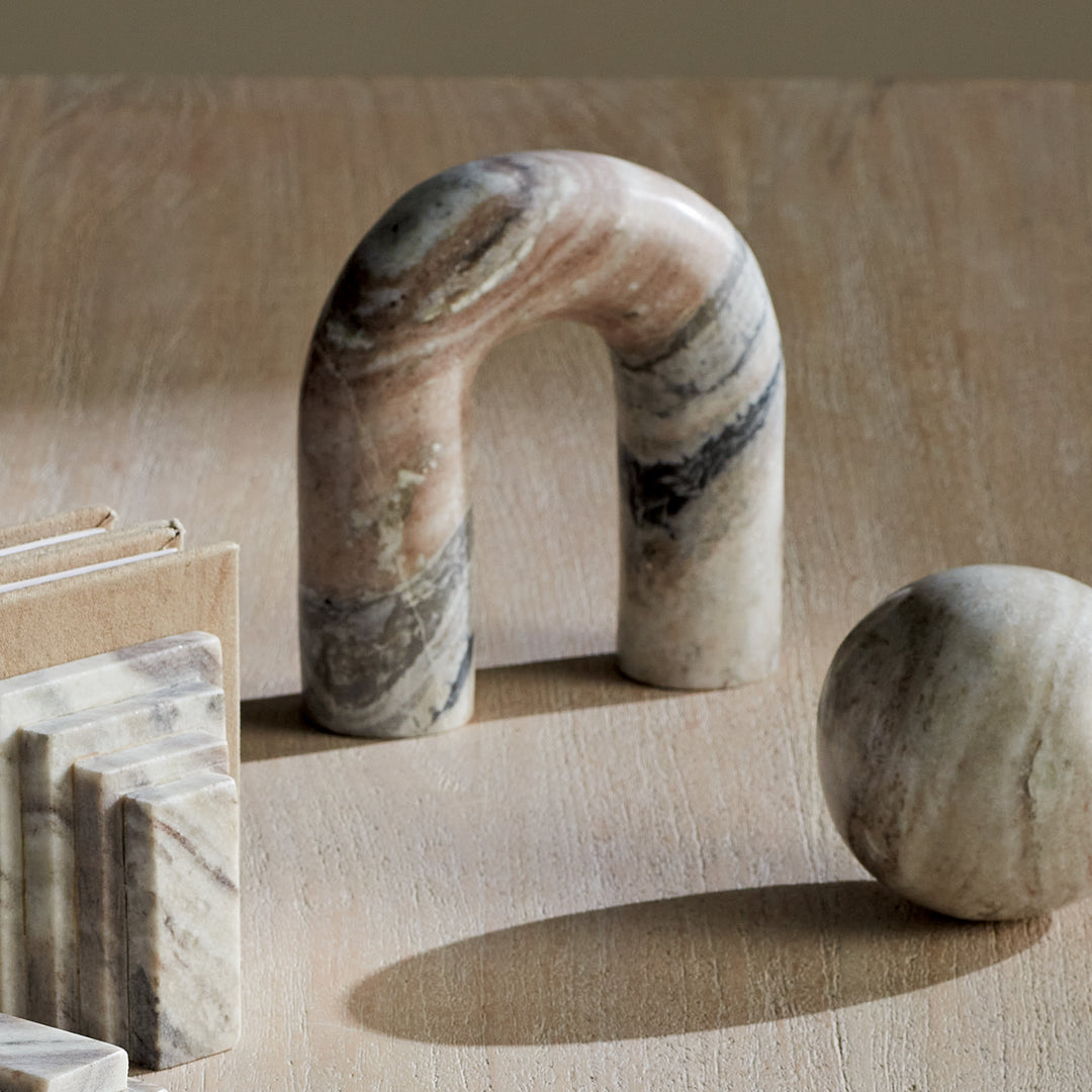 Brown and white marble arch sculpture on a wood tabletop beside a matching orb, with books at the scene edge. Modern Organic