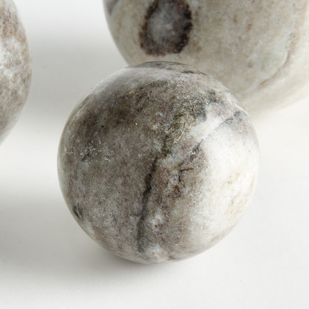 Close view of a brown and white marble orb with layered veining, with other graduated stone spheres behind. Modern Organic