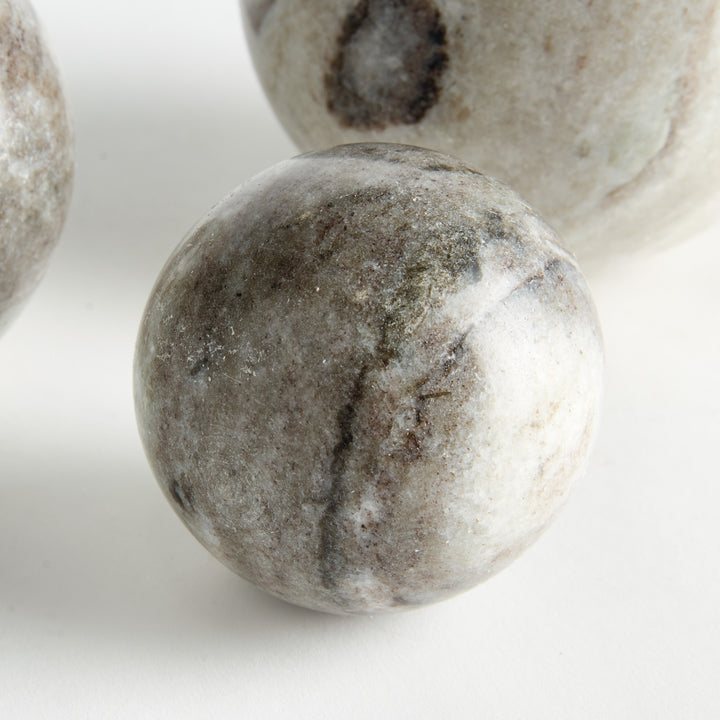 Close view of a brown and white marble orb with layered veining, with other graduated stone spheres behind. Modern Organic