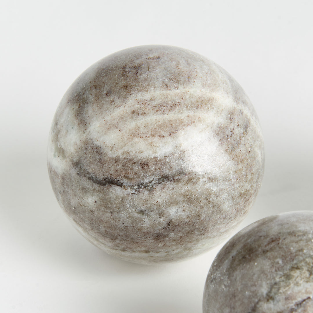 Close view of a marble orb with broad brown and white bands, beside part of another matching stone sphere. Modern Organic