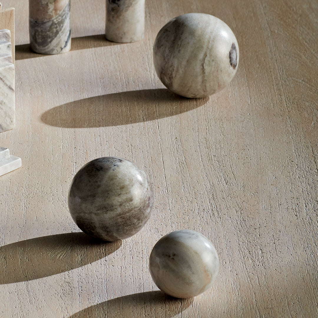 Brown and white marble orbs on a wood tabletop beside an arch sculpture, showing graduated sizes and veining. Modern Organic