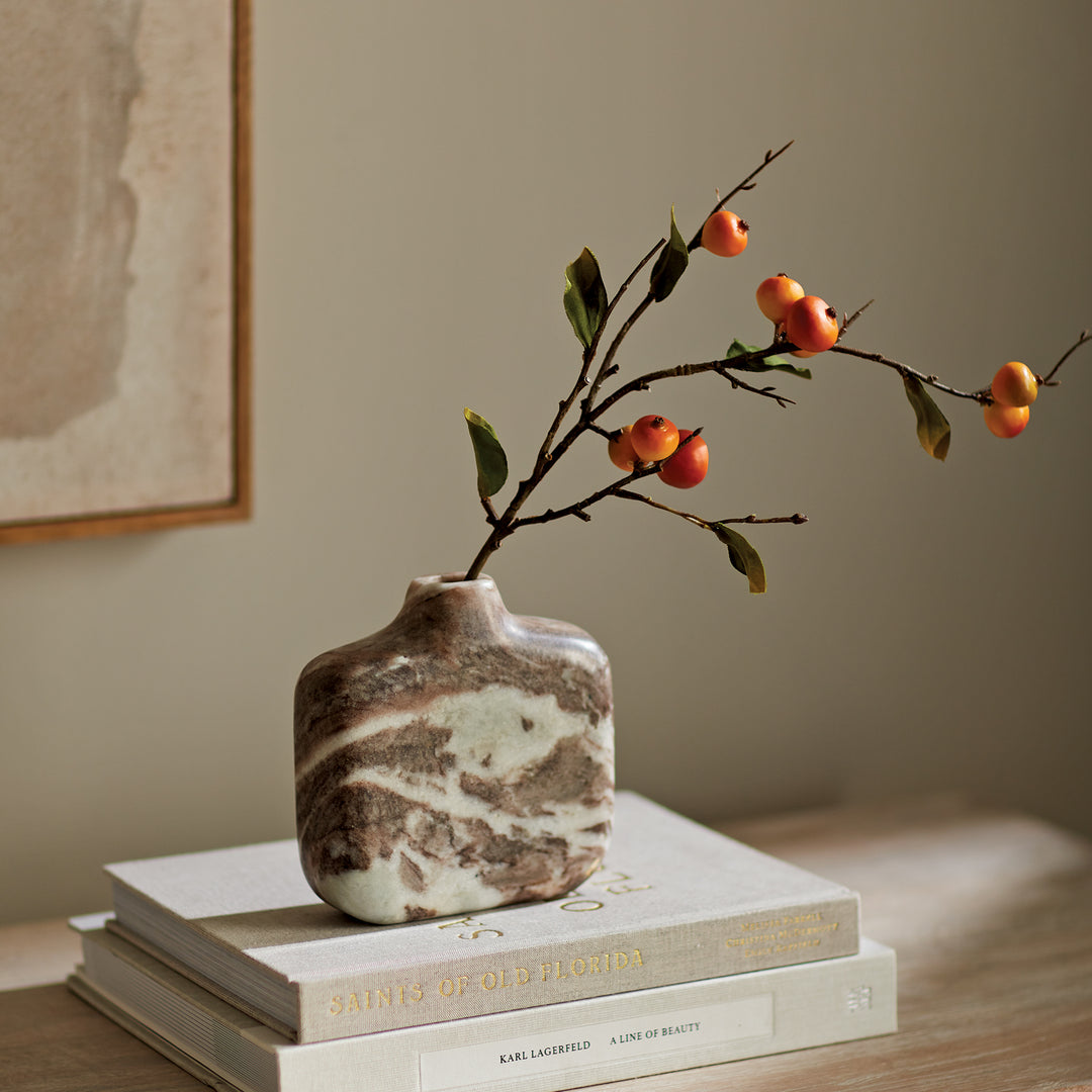 Brown and white marble vase on stacked books with fruiting branch, showing its flattened body and short neck. Modern Organic