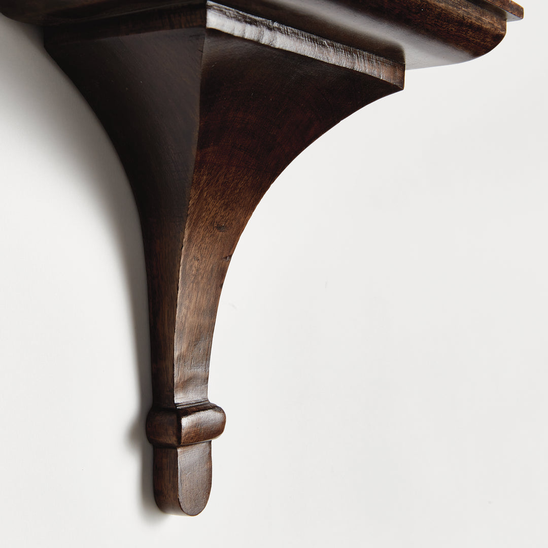 Close-up of sculpted bracket curve in antique brown finish, highlighting silhouette and handcrafted mango wood texture.

