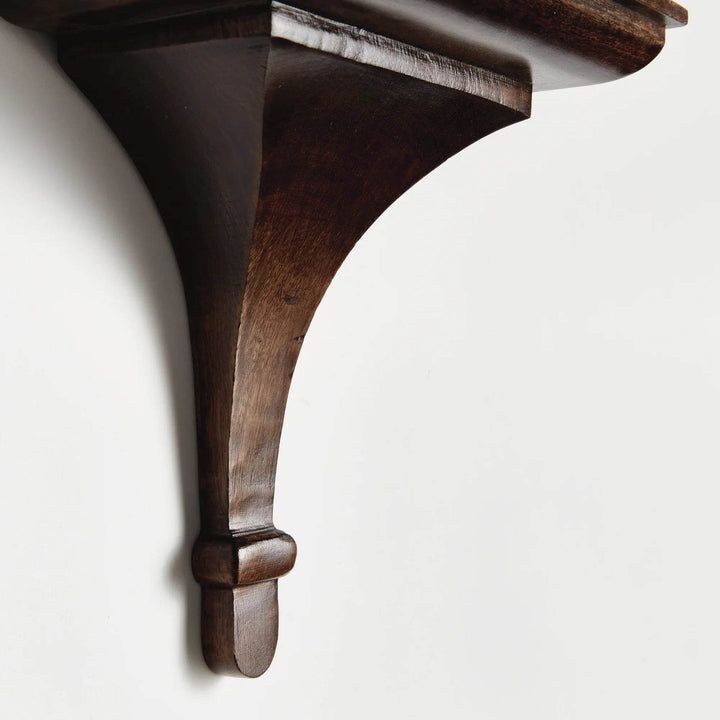 Close-up of sculpted bracket curve in antique brown finish, highlighting silhouette and handcrafted mango wood texture.

