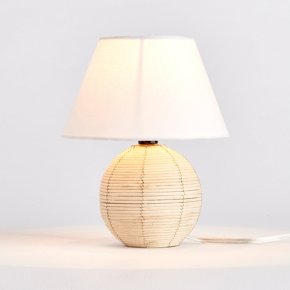 Handcrafted with natural cane rattan, every mini table lamp displays unique variations in color, making it truly one-of-a-kind. Its compact size and refined cotton blend shade make it an ideal choice for kitchens or small workspaces. Featuring natural tones and rattan material, it is a perfect addition to any bedroom.