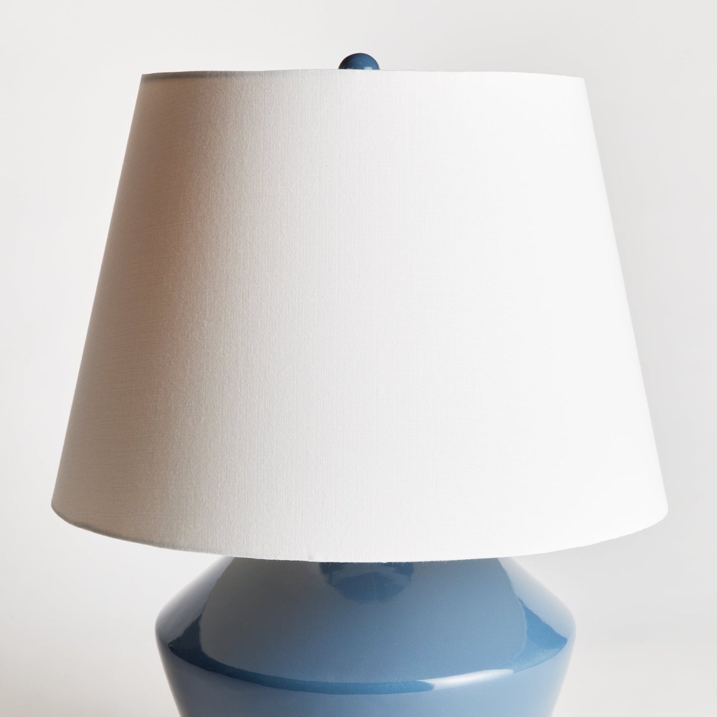 Crafted from a wooden mold dating back centuries, this stunning table lamp boasts a timeless silhouette and a deep blue finish. Topped with a tapered fabric shade, it adds a touch of history and elegance to any room, whether it be a family room, study, or bedroom. This ceramic blue table lamp is a dynamic addition to any space.