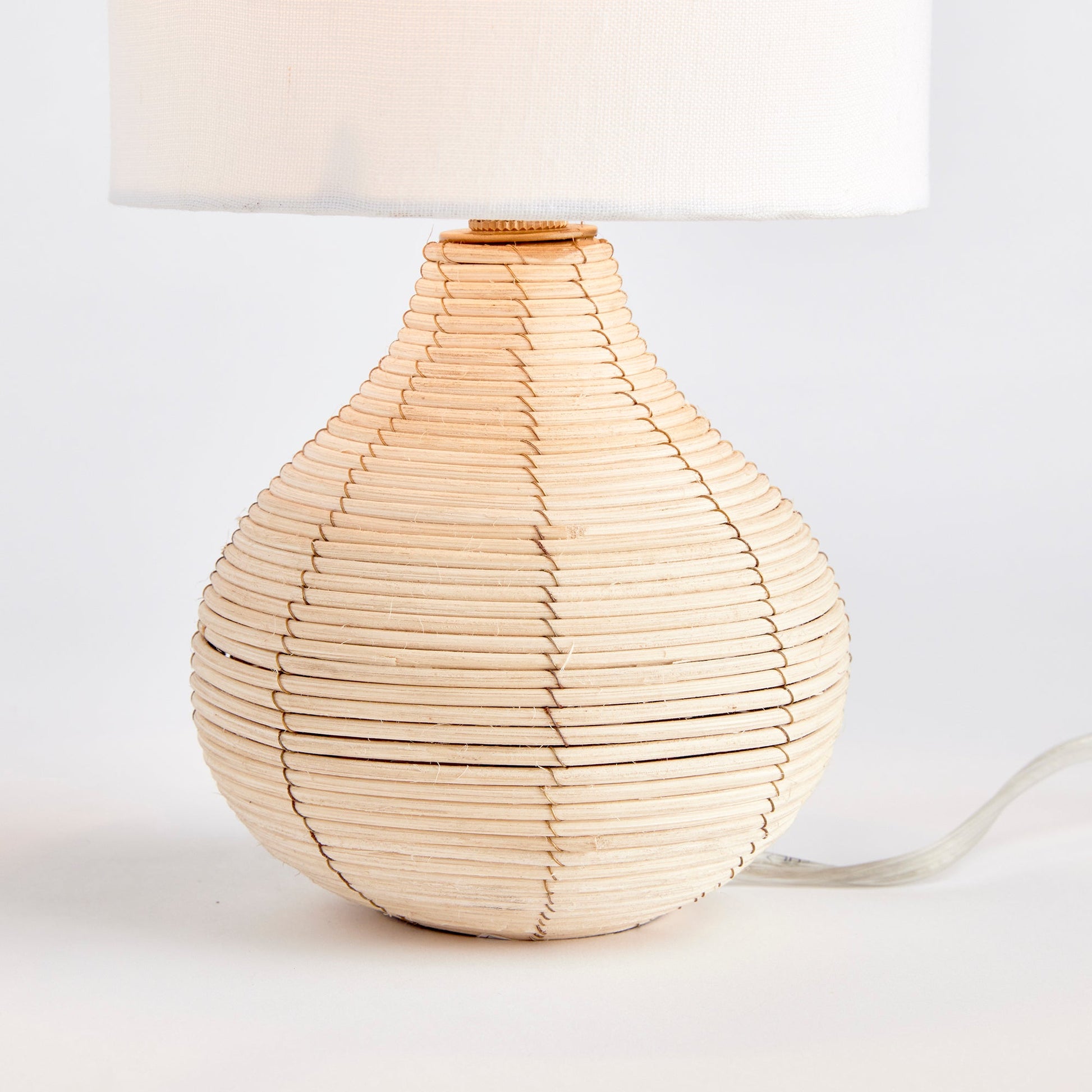 This table lamp is the perfect addition to any kitchen or small workspace, thanks to its petite shape and tailored shade. Crafted with a natural cane rattan base and a linen shade, it exudes a casual yet elegant feel. Its one-of-a-kind design showcases the use of rattan, jute, and cotton in the shade, while the candelabra bulb adds a touch of uniqueness.