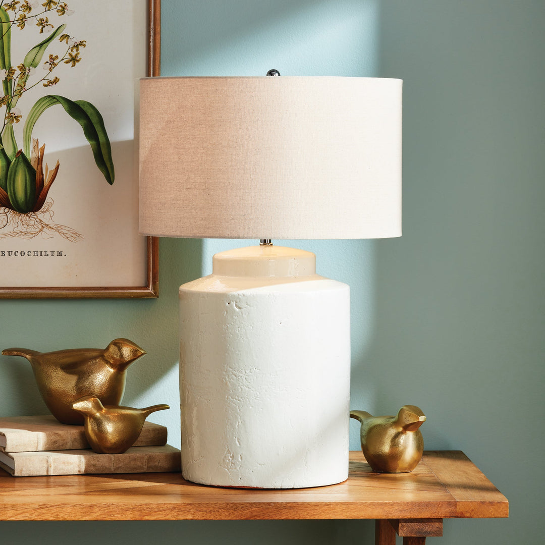 This Monty White Transitional Table Lamp is crafted from elegant white ceramic with a thick glaze, making it a perfect addition to transitional décor. Its generously-sized white linen shade and sleek finial add a touch of sophistication to its timeless design. The table lamp's construction is elegant and durable, creating a lasting beauty that will elevate any space. Add character and style to any room with this versatile and sophisticated lamp.