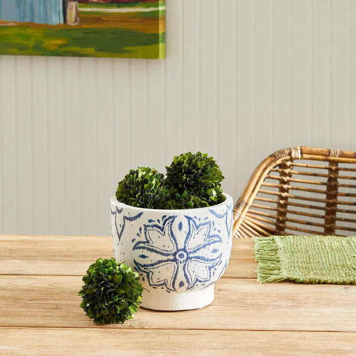 Blue and white ceramic cachepot planter styled with faux boxwood drop-ins on wood tabletop – Coastal Casual.

