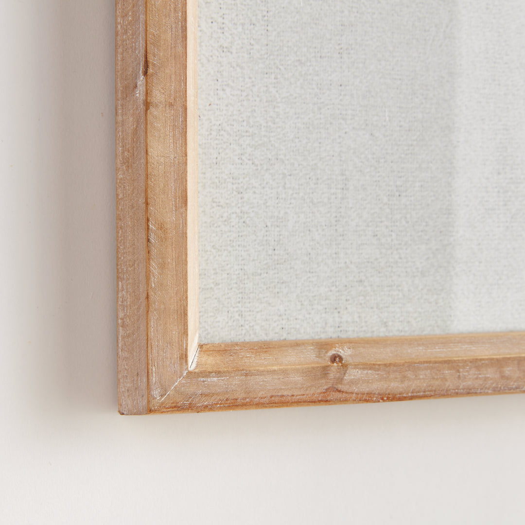 Close detail of the natural wood frame corner around a blue coral print, showing pale artwork behind glass covering. Coastal