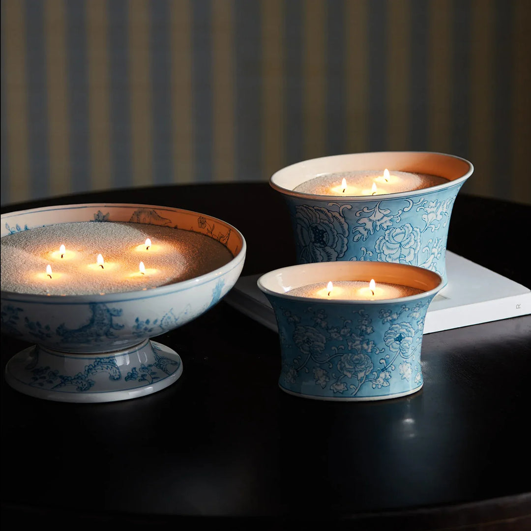 Candle sand styled in decorative blue and white vessels creating layered candlelight ambiance on tabletop display
