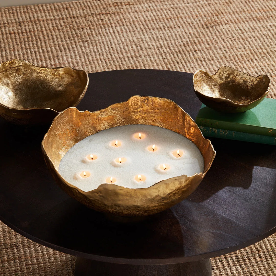 White candle sand displayed in sculptural brass bowl with multiple wicks creating warm glowing centerpiece lighting
