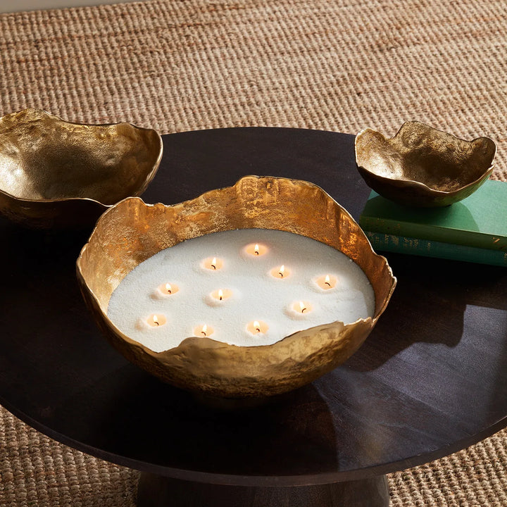 White candle sand displayed in sculptural brass bowl with multiple wicks creating warm glowing centerpiece lighting