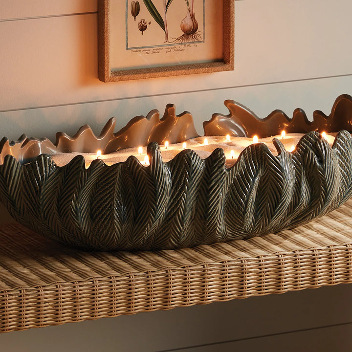 Close-up of candle sand in large sculptural leaf vessel showing multiple lit wicks and soft glowing wax surface