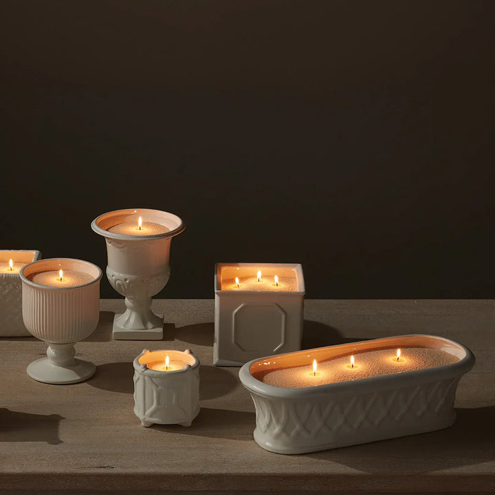 Candle sand displayed across white ceramic vessels in various shapes creating cohesive multi-candle tabletop arrangement