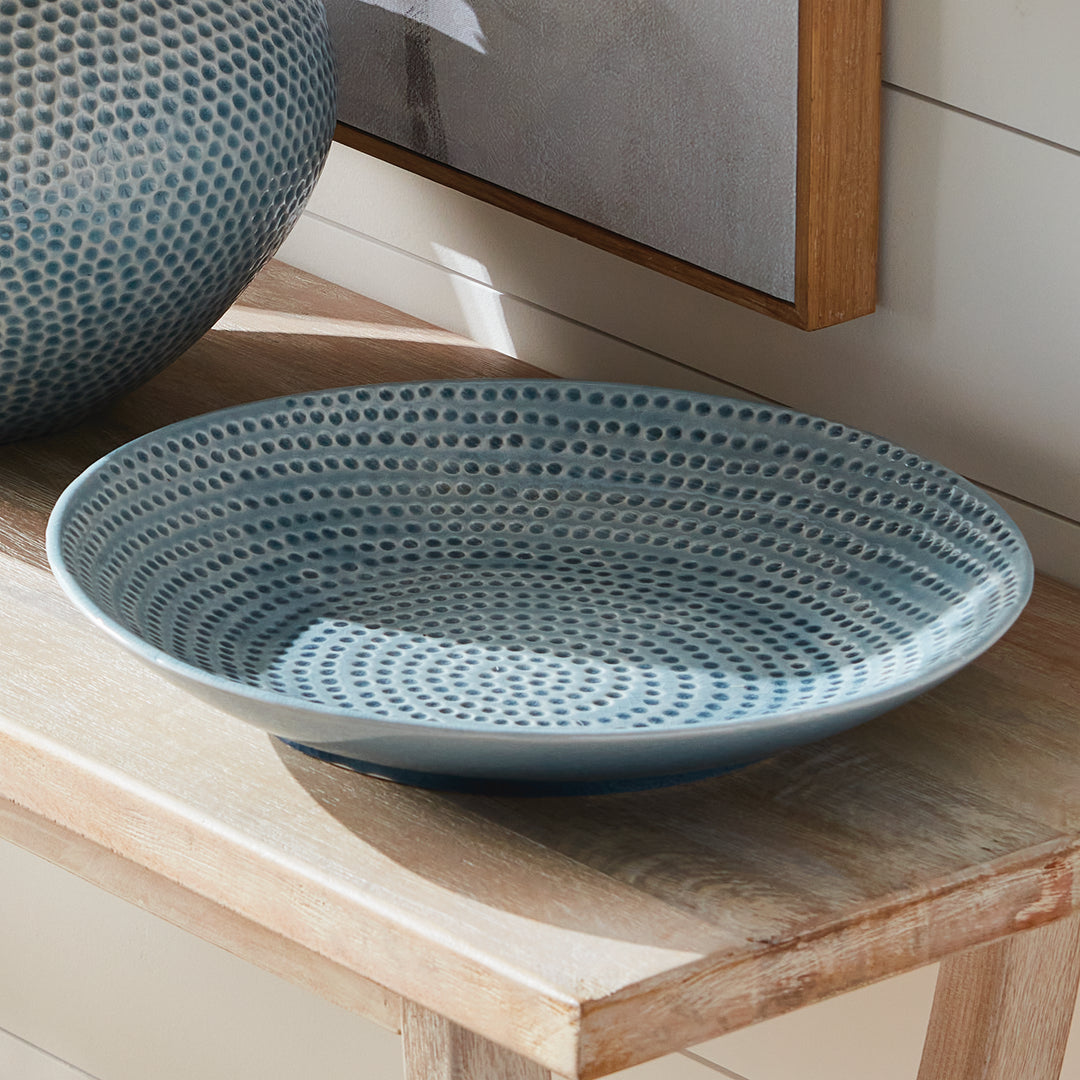 Carys blue decorative plate on a wood console beside a matching rounded vase and framed artwork in natural light. Coastal