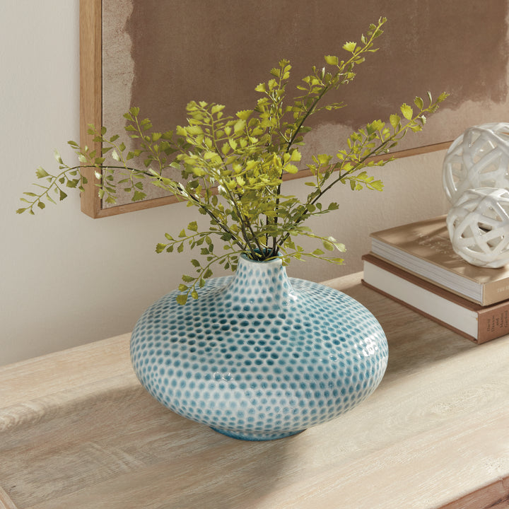 Carys low blue vase with leafy green stems on a wood console beside books and white openwork decorative spheres. Coastal