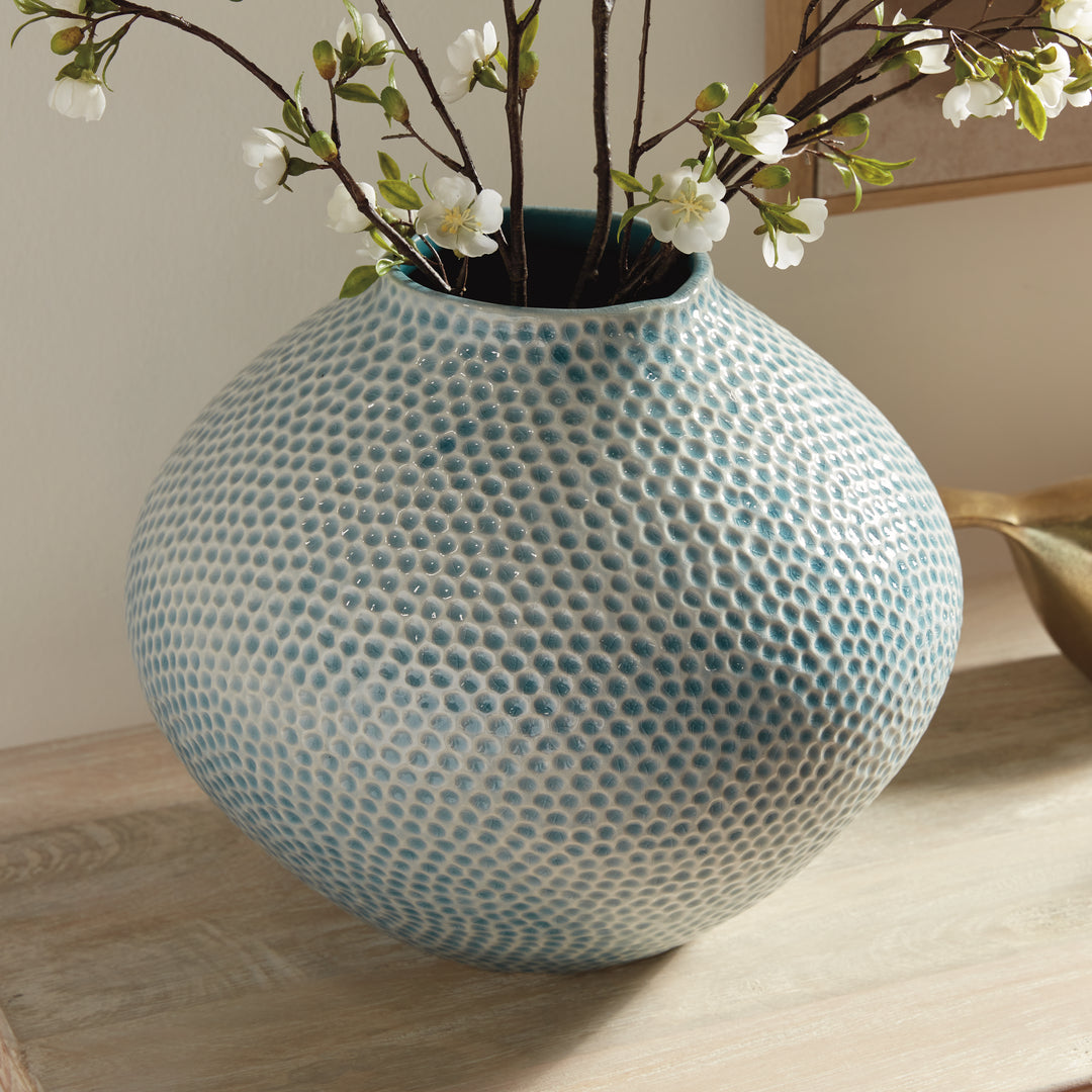 Detail of Carys rounded blue clay vase showing the textured glazed body below white flowering branches on a console. Coastal