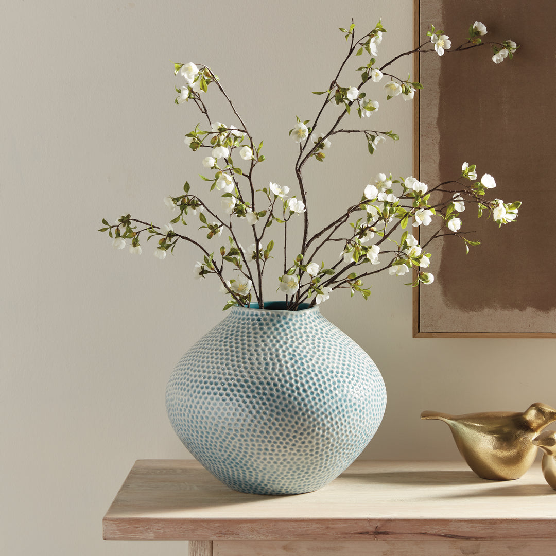 Carys rounded blue dimpled vase with white flowering branches on a wood console beside gold birds and framed artwork. Coastal