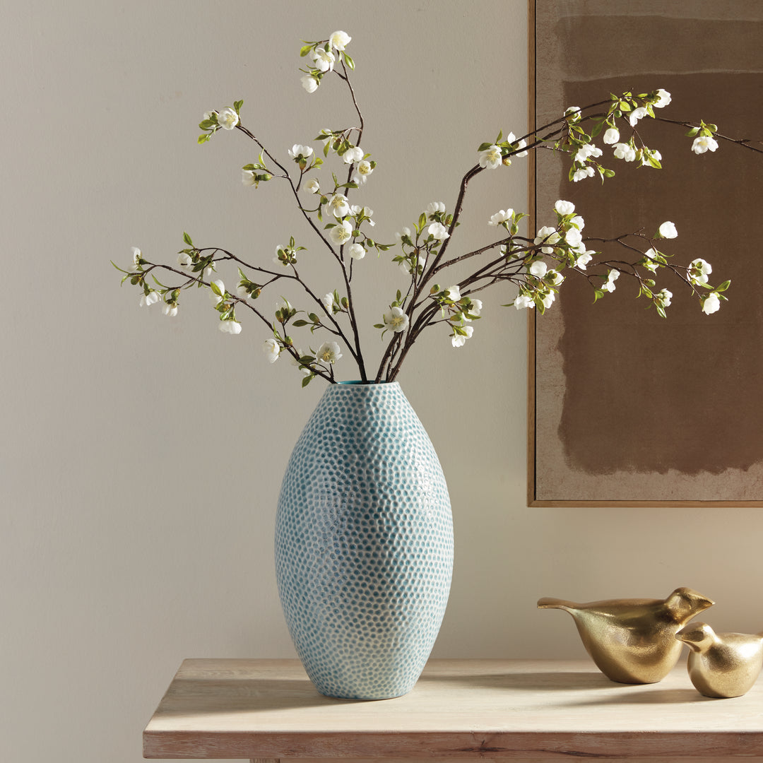 Carys tall blue dimpled vase with white flowering branches on a console beside gold bird sculptures and framed art. Coastal