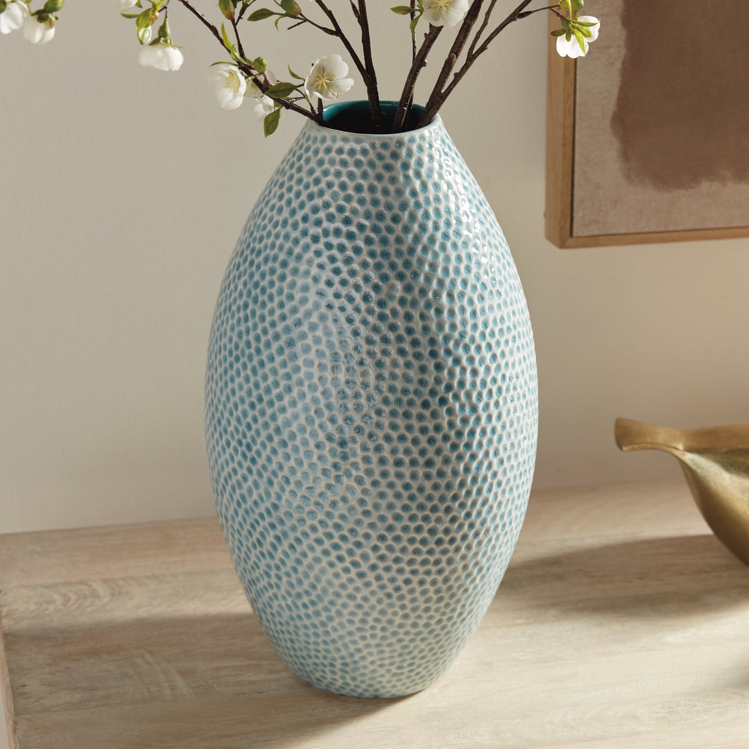 Detail of Carys tall blue vase with flowering branches showing its glazed dotted surface beside a gold bird accent. Coastal