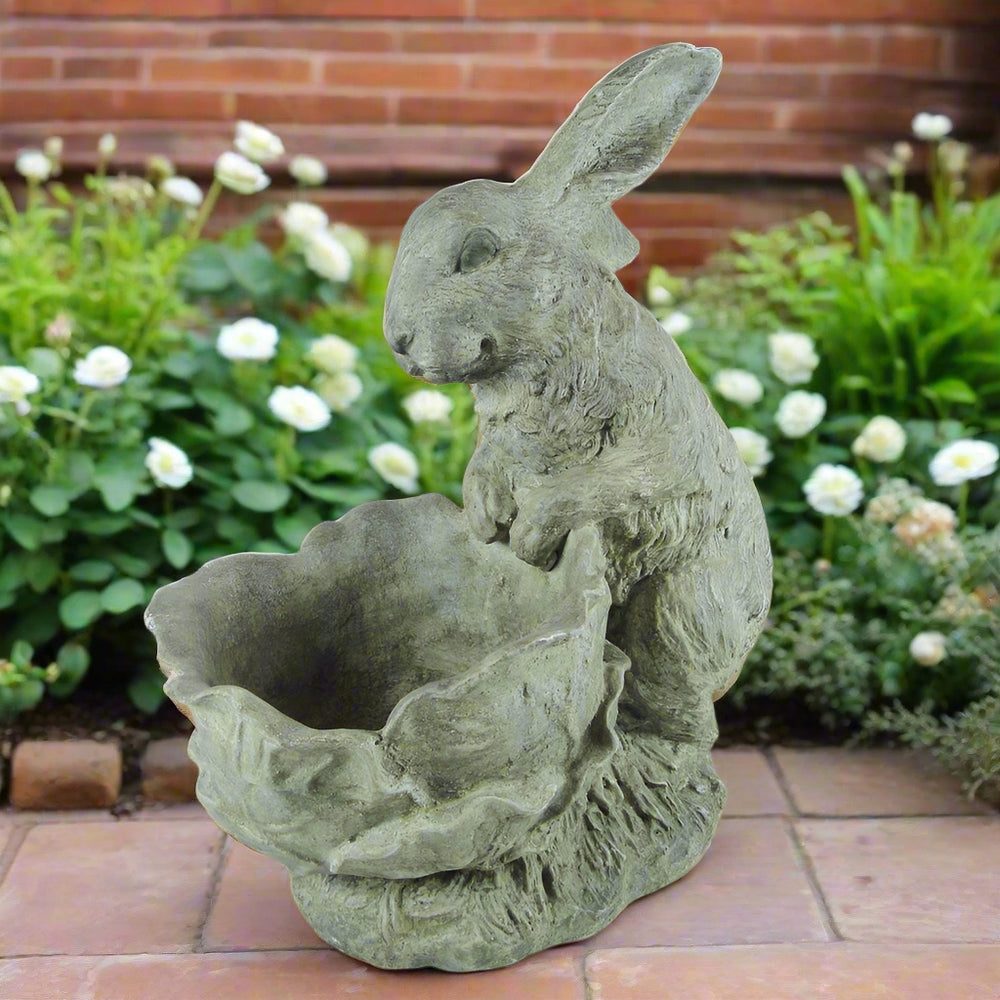 Decorative cement bunny planter in a flowering garden surrounded by white blooms and greenery
