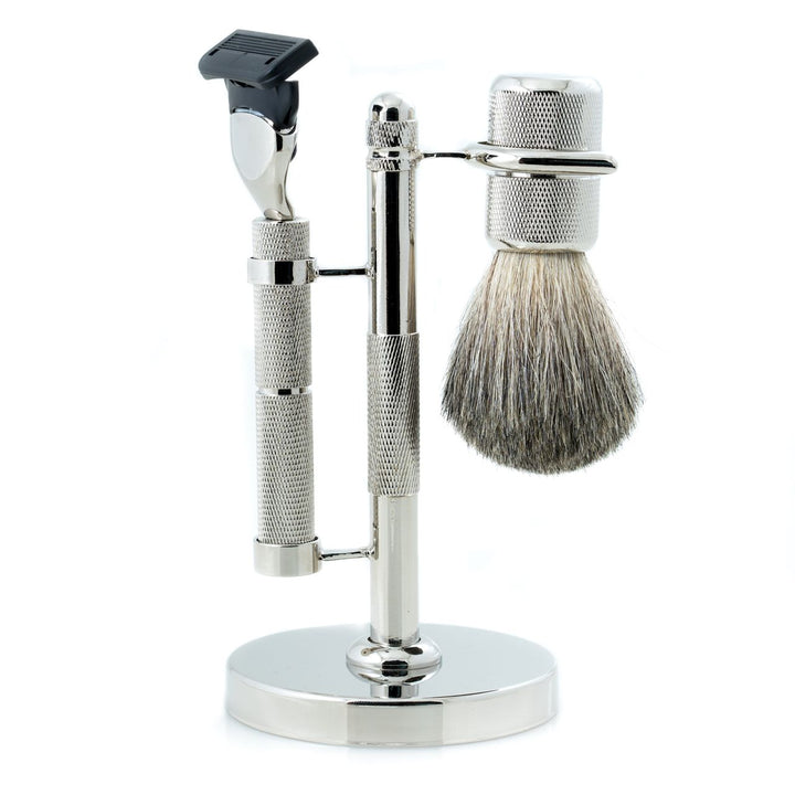 Side view of chrome razor and pure badger brush three-piece shaving set with diamond-cut textured handles and chrome stand, one blade installed.