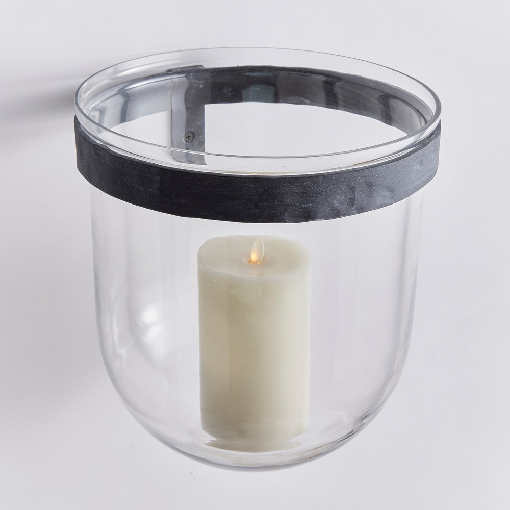Angled view of clear glass wall candle holder with rounded glass base, aged zinc band and LED pillar candle in Modern Organic