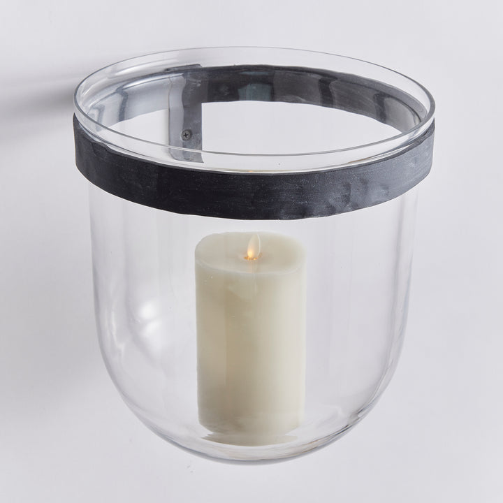 Angled view of clear glass wall candle holder with rounded glass base, aged zinc band and LED pillar candle in Modern Organic