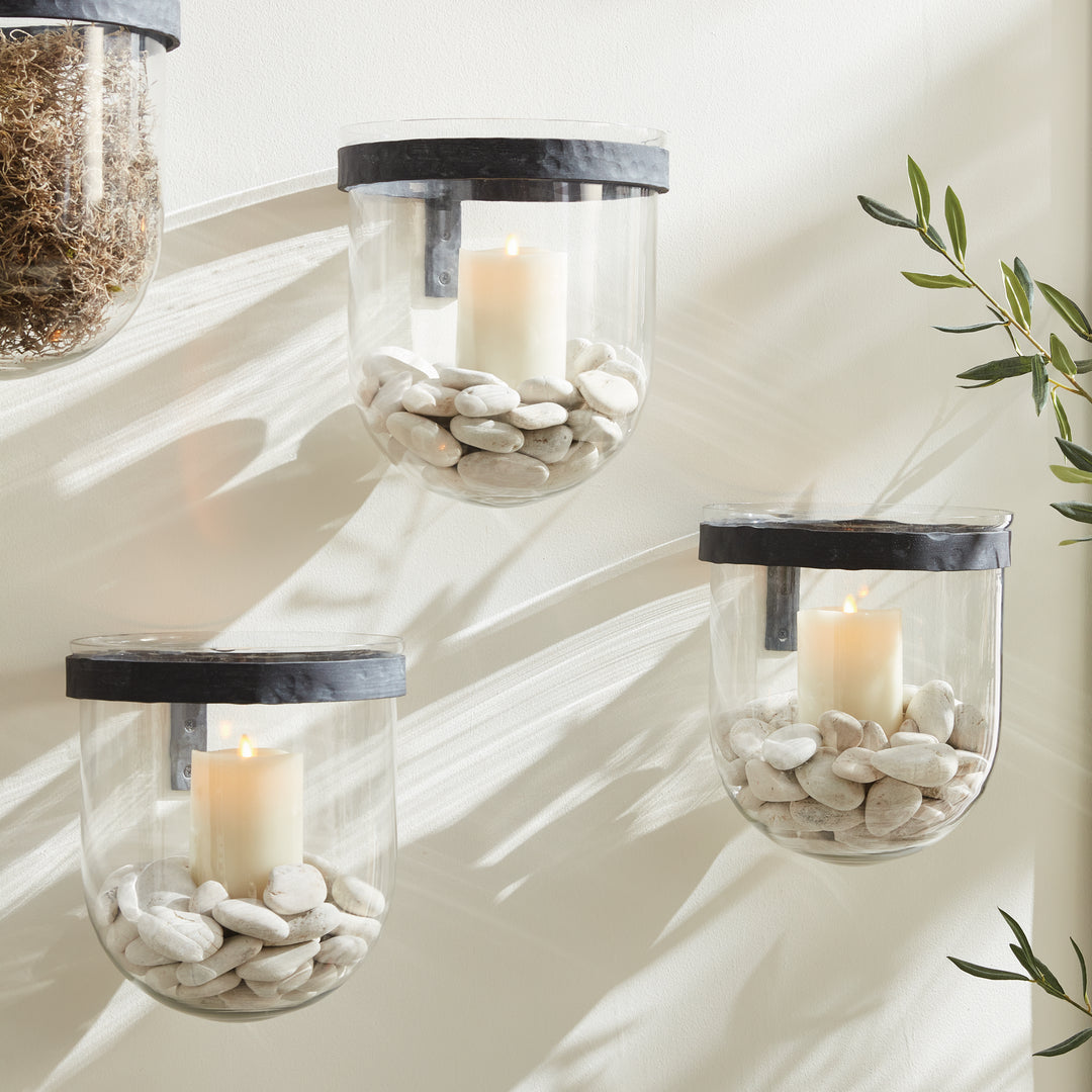 Grouped glass wall candle holders with aged zinc bands, LED candles and smooth pale pebbles on a light wall in Modern Organic
