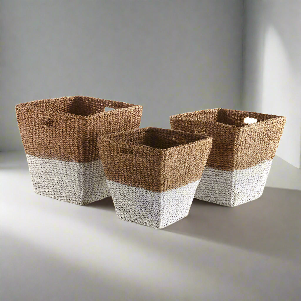 Set of three seagrass baskets styled together on a neutral rug in a coastal farmhouse interior with soft light.