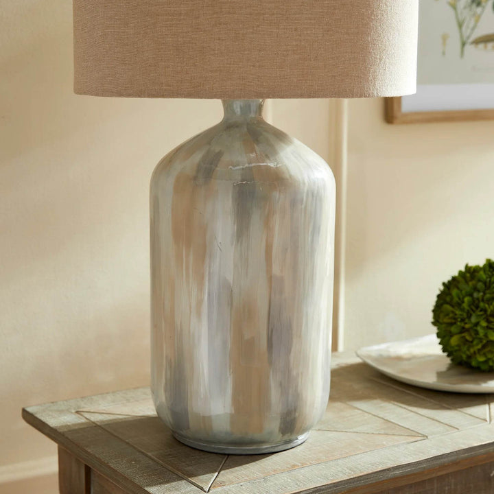 Side view of coastal-style neutral table lamp with creamy brushstroke finish on console with soft lighting and artwork.

